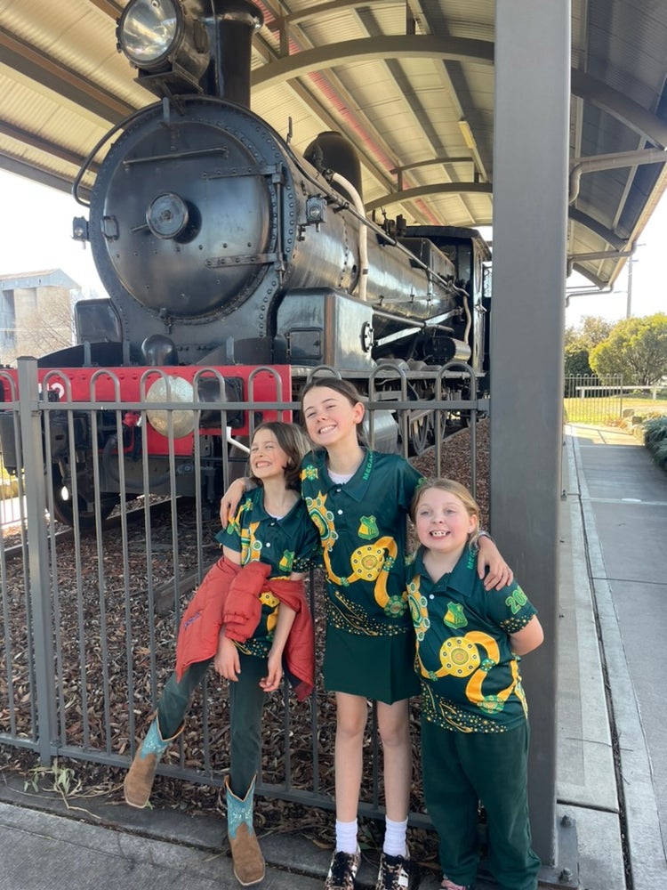 Students at railway museum posing in front of old steam train