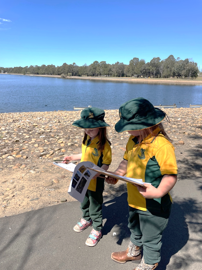 2 students walking on a path beside a lake